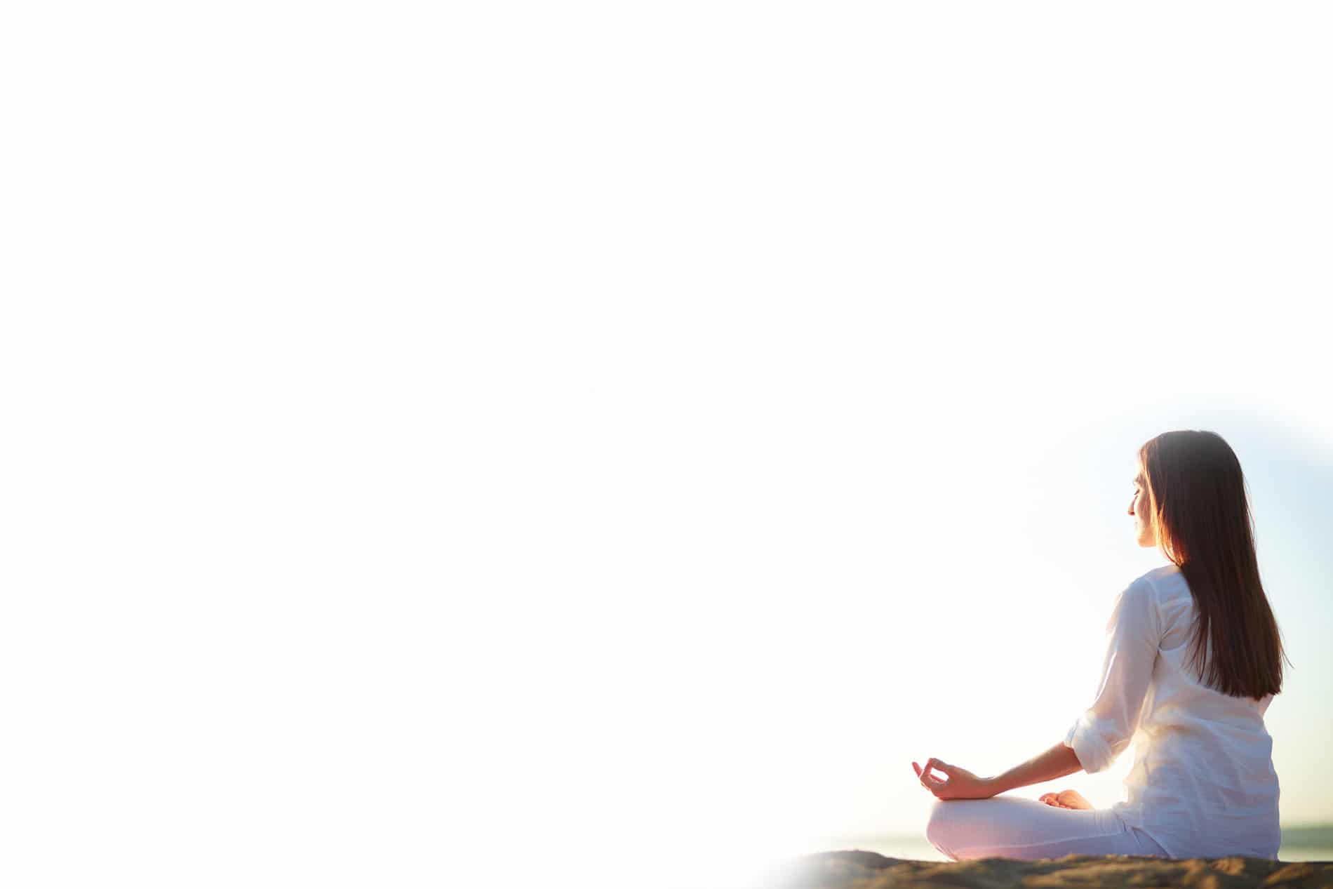 A woman meditating cross-legged on a hilltop at sunrise
